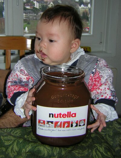 Katja sitzt nutella-verschmiert vor einem großen nutella-Glas